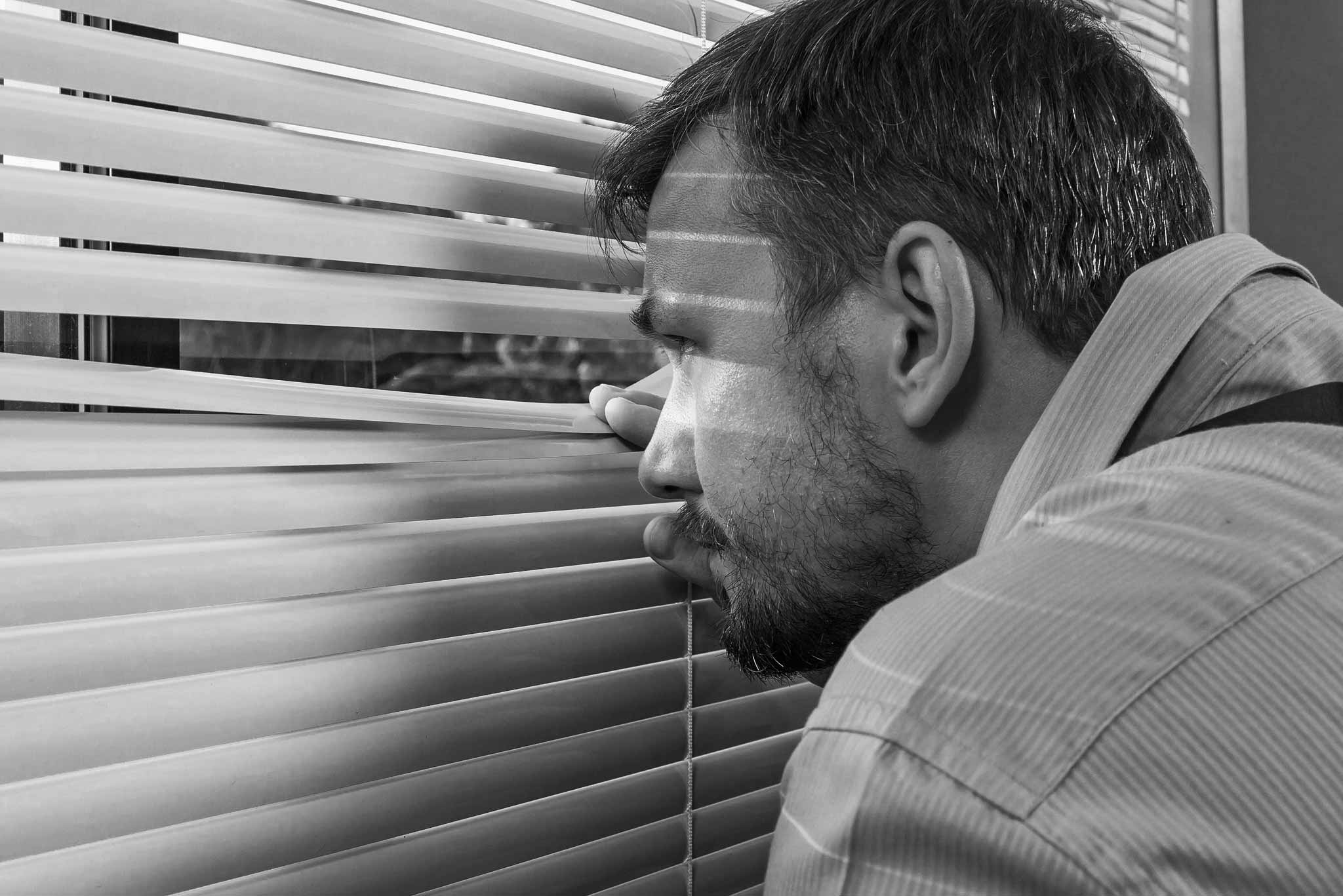 paranoid man looking through window blinds showing one sing of how to tell if someone is on meth