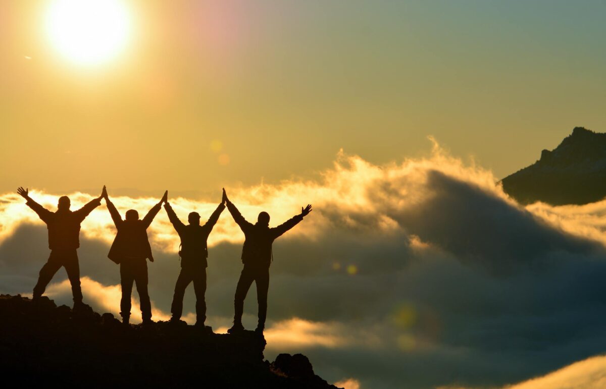 four people reaching the top of a mountain celebrating reaching success benchmarks in a transitional living program